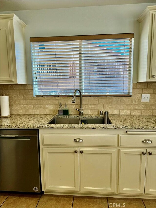 kitchen with a sink, backsplash, stainless steel dishwasher, and light stone countertops