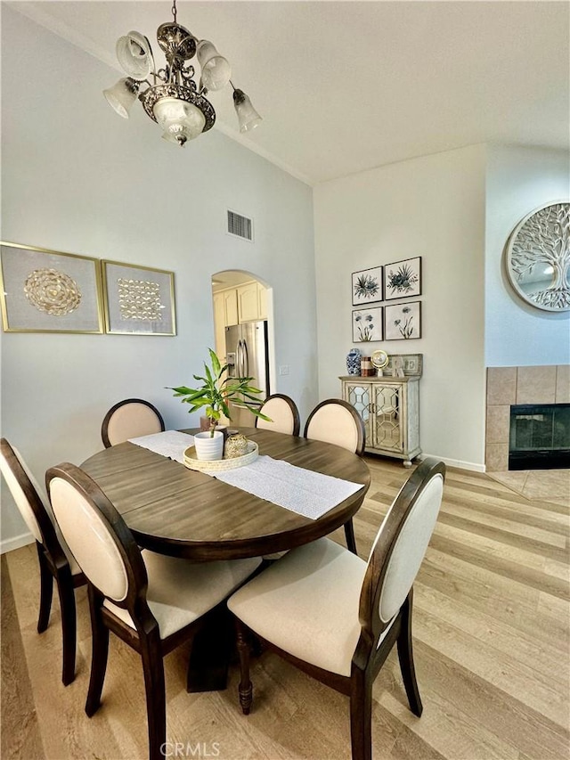 dining area featuring a chandelier, arched walkways, visible vents, light wood-style floors, and a tiled fireplace