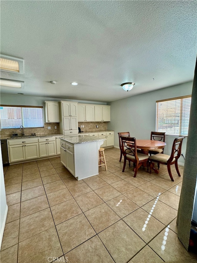 kitchen featuring light stone countertops, tasteful backsplash, light tile patterned floors, white cabinets, and a kitchen island