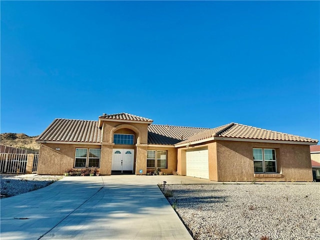 mediterranean / spanish-style house with a tiled roof, an attached garage, and stucco siding