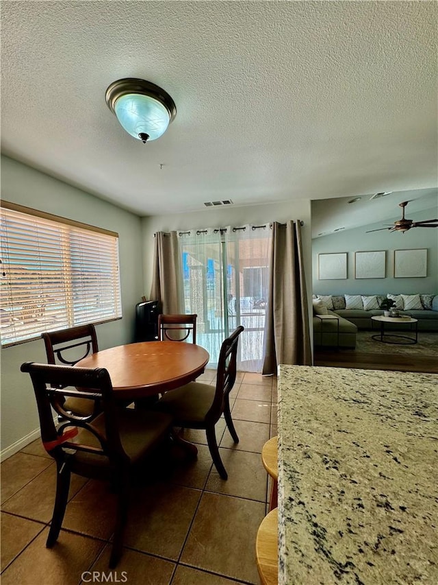 tiled dining space with visible vents, ceiling fan, a textured ceiling, and baseboards