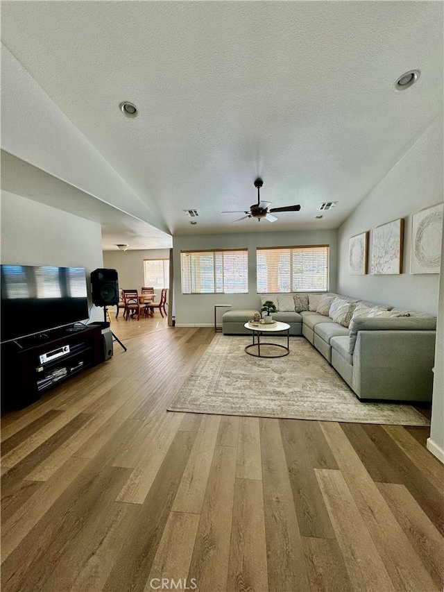 living room with vaulted ceiling, ceiling fan, light hardwood / wood-style flooring, and a textured ceiling