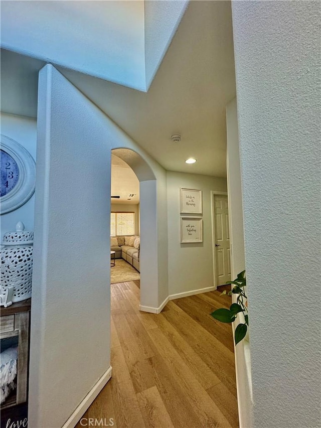 hall featuring baseboards, arched walkways, wood finished floors, and a textured wall