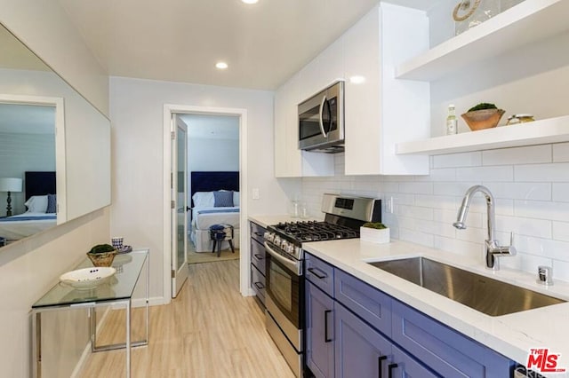 kitchen with appliances with stainless steel finishes, light wood-type flooring, light stone counters, blue cabinets, and sink