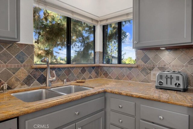 kitchen featuring decorative backsplash, sink, gray cabinetry, and light stone countertops