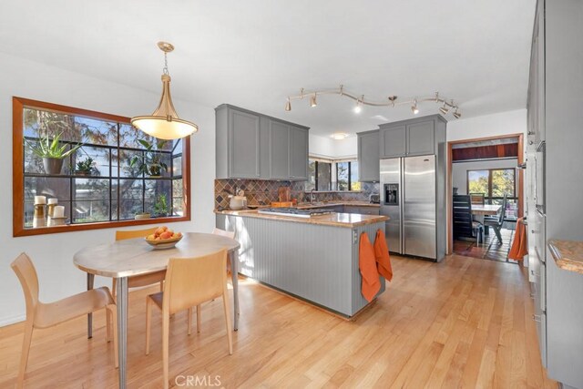 kitchen with stainless steel refrigerator with ice dispenser, tasteful backsplash, plenty of natural light, light wood-type flooring, and gray cabinetry