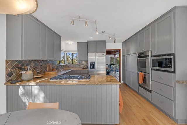 kitchen featuring kitchen peninsula, tasteful backsplash, gray cabinets, light hardwood / wood-style floors, and stainless steel appliances