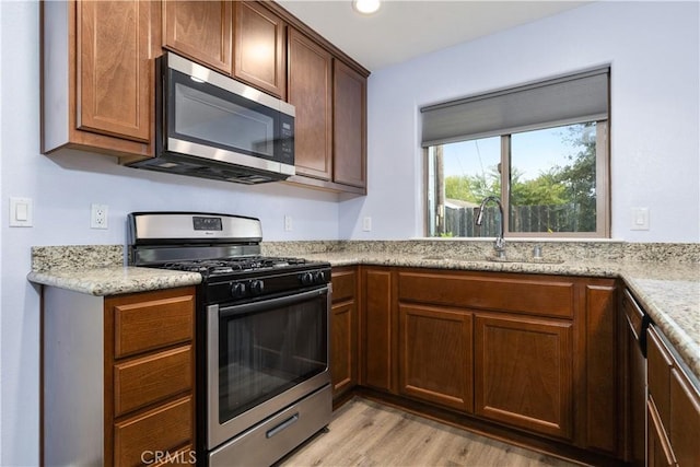 kitchen with light stone countertops, sink, appliances with stainless steel finishes, and light hardwood / wood-style flooring