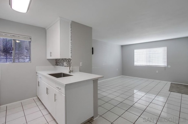 kitchen with kitchen peninsula, light tile patterned floors, white cabinetry, and sink