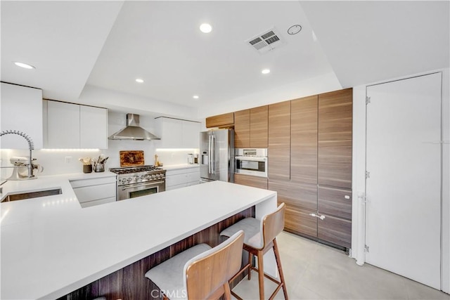 kitchen featuring white cabinetry, sink, wall chimney exhaust hood, a kitchen bar, and appliances with stainless steel finishes