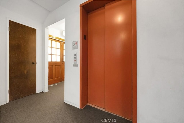 hall with dark colored carpet and elevator