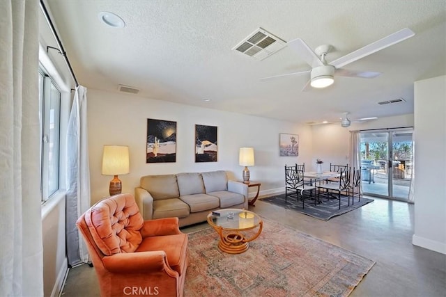 living room with ceiling fan, a textured ceiling, and concrete floors