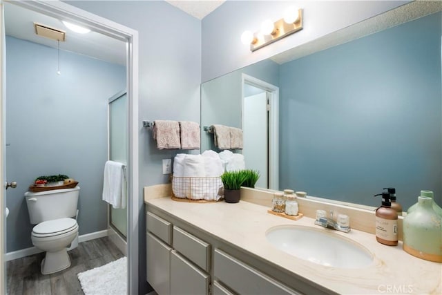 bathroom with hardwood / wood-style floors, vanity, a shower with door, and toilet