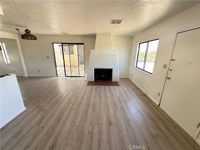 unfurnished living room with a large fireplace, light hardwood / wood-style floors, and a textured ceiling