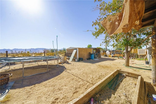 view of yard featuring a mountain view, a trampoline, and a storage unit