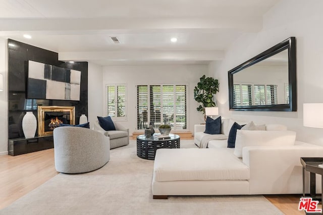 living room featuring beam ceiling, a tiled fireplace, and hardwood / wood-style floors