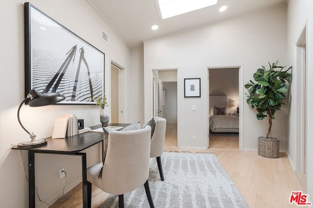 office featuring lofted ceiling with skylight and light hardwood / wood-style flooring