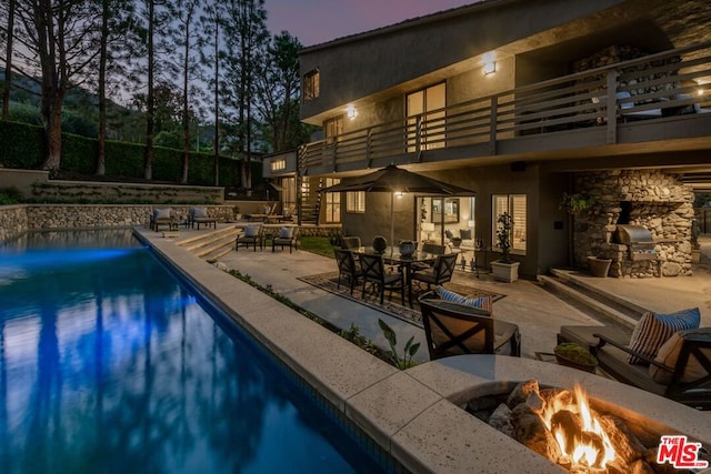 pool at dusk with an outdoor fire pit and a patio