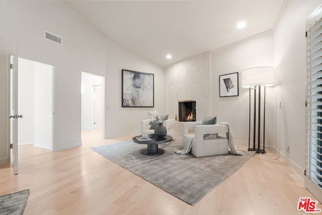 living area featuring high vaulted ceiling, a tile fireplace, and light wood-type flooring