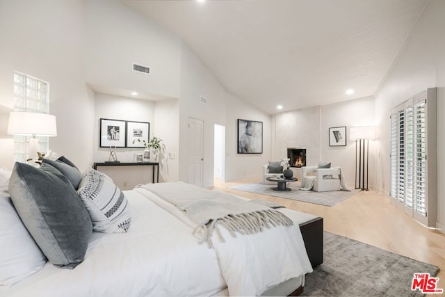 bedroom featuring high vaulted ceiling, light hardwood / wood-style flooring, and a fireplace