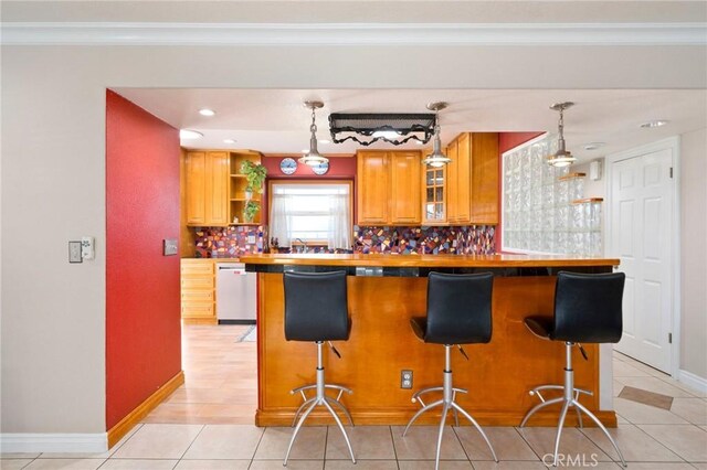 kitchen featuring stainless steel dishwasher, decorative light fixtures, decorative backsplash, a breakfast bar, and light tile patterned flooring