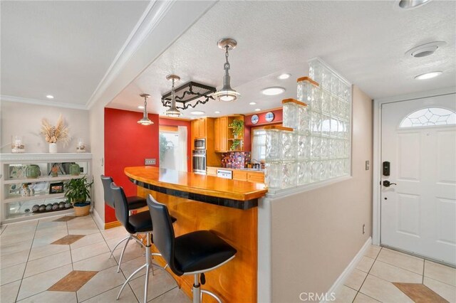 kitchen featuring light tile patterned floors, a textured ceiling, hanging light fixtures, and crown molding