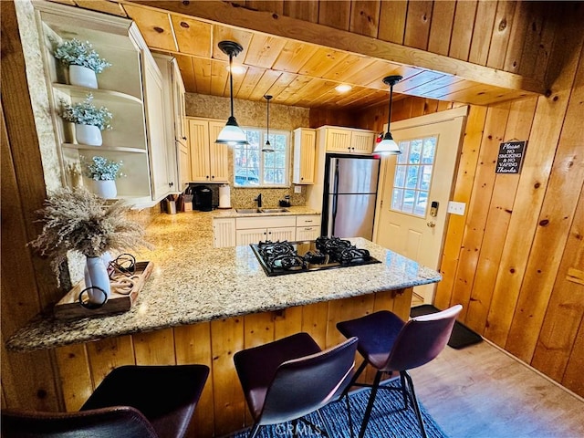 kitchen featuring a breakfast bar, freestanding refrigerator, a peninsula, pendant lighting, and black gas stovetop