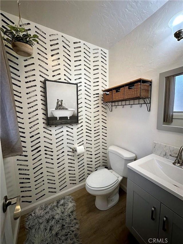 bathroom featuring a textured ceiling, a textured wall, toilet, wood finished floors, and vanity