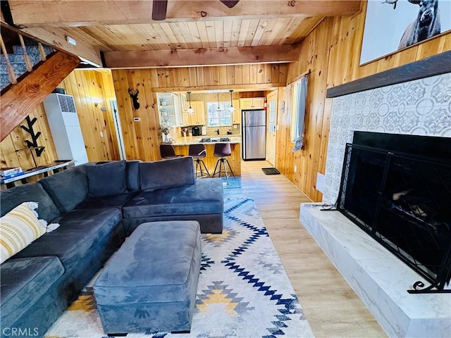 living room with wood ceiling, wood walls, light wood-type flooring, beamed ceiling, and a tile fireplace