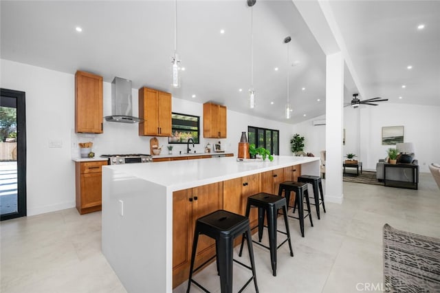 kitchen featuring ceiling fan, a kitchen breakfast bar, hanging light fixtures, vaulted ceiling, and wall chimney exhaust hood