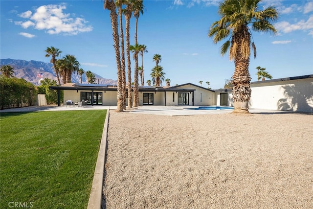 rear view of house featuring a mountain view, a patio area, a lawn, roof mounted solar panels, and stucco siding