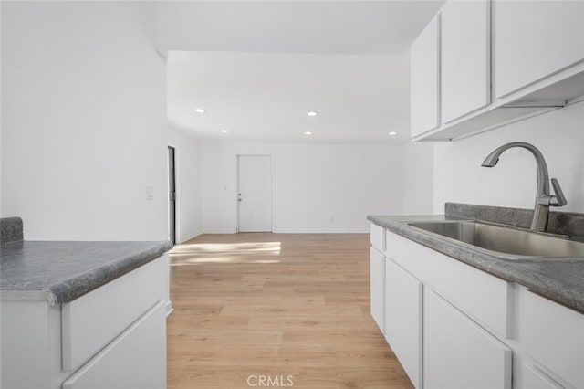 kitchen featuring white cabinets, recessed lighting, light wood finished floors, dark countertops, and a sink