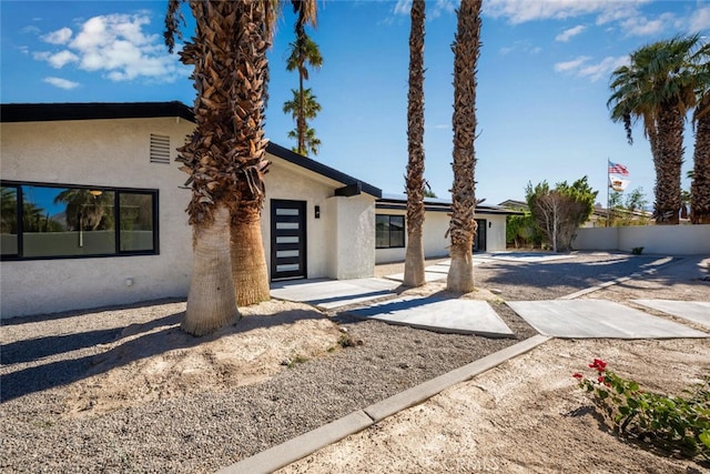 view of front of home featuring roof mounted solar panels, fence, and stucco siding