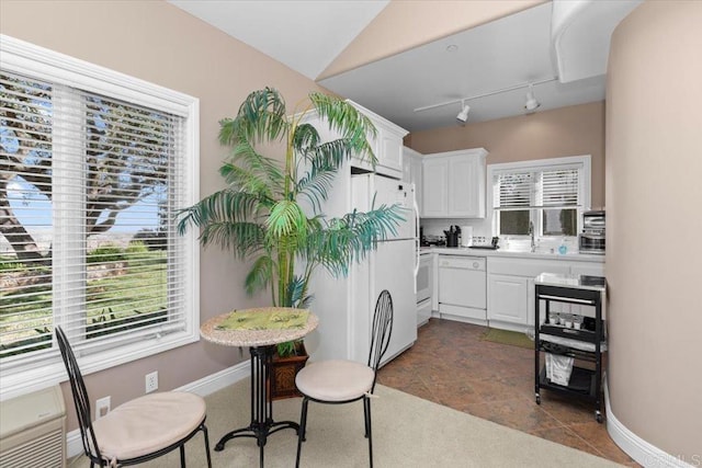 kitchen with track lighting, white appliances, vaulted ceiling, sink, and white cabinets