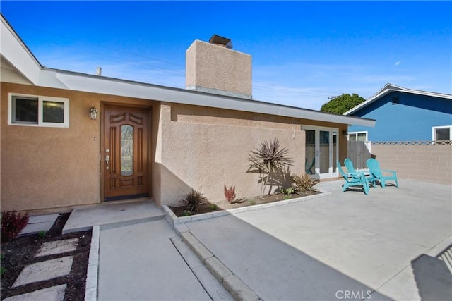 doorway to property with stucco siding, fence, and a patio