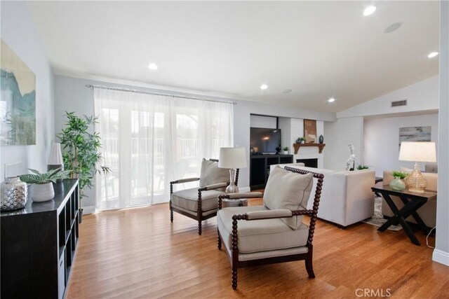 living room with vaulted ceiling, a large fireplace, and light wood-type flooring