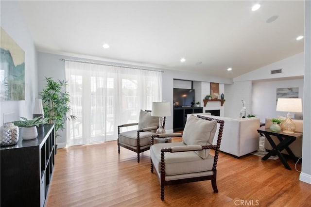 living area featuring lofted ceiling, recessed lighting, a fireplace, visible vents, and light wood-type flooring