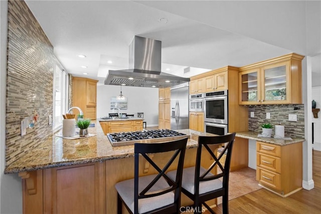 kitchen with a peninsula, stainless steel appliances, glass insert cabinets, tasteful backsplash, and island range hood