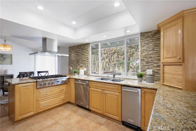 kitchen with island range hood, appliances with stainless steel finishes, a peninsula, light stone countertops, and a sink