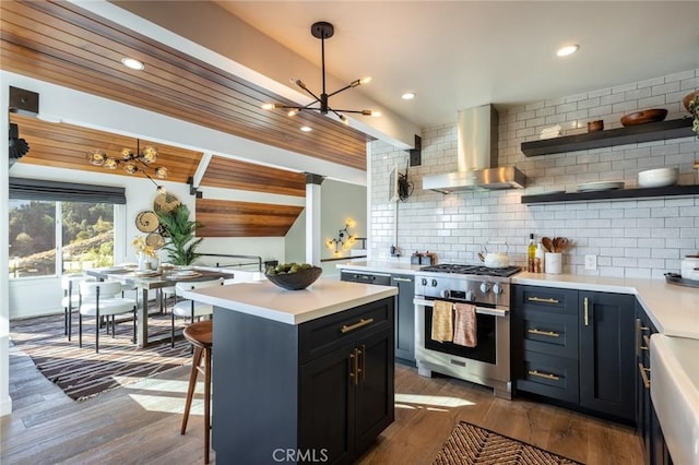 kitchen with hardwood / wood-style floors, pendant lighting, wall chimney range hood, high end stainless steel range oven, and decorative backsplash