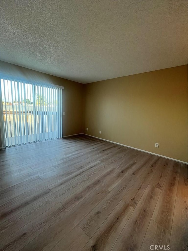 empty room with a textured ceiling and light hardwood / wood-style flooring