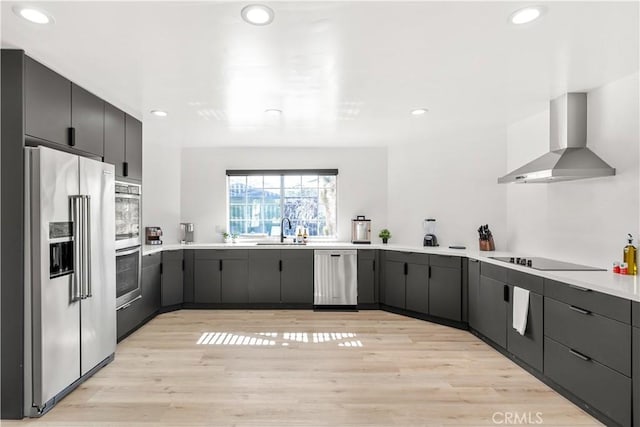 kitchen with sink, stainless steel appliances, wall chimney range hood, and light wood-type flooring