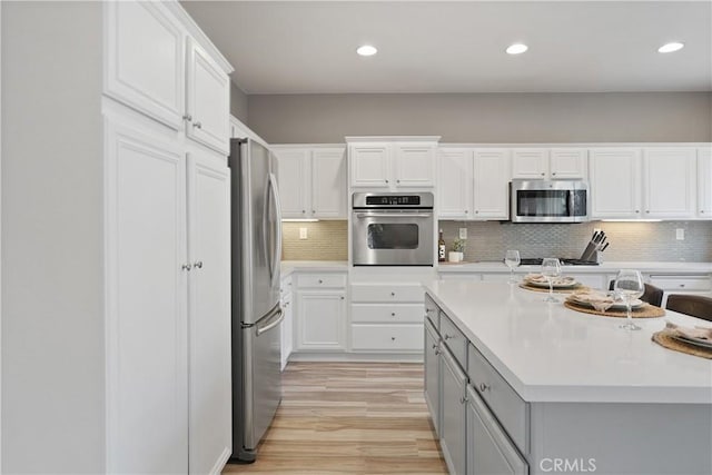 kitchen with backsplash, white cabinetry, light hardwood / wood-style flooring, and stainless steel appliances