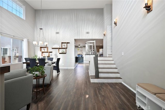 living room featuring dark hardwood / wood-style flooring, ceiling fan with notable chandelier, and a high ceiling