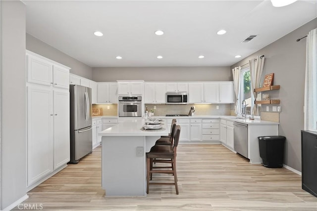 kitchen featuring a center island, light hardwood / wood-style floors, a kitchen bar, white cabinetry, and stainless steel appliances