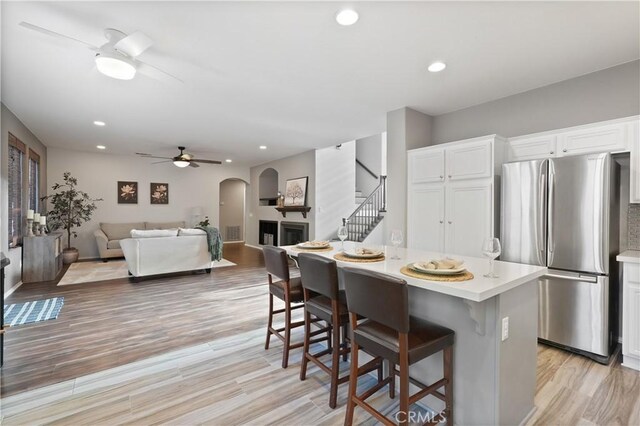 kitchen with a kitchen bar, light wood-type flooring, a kitchen island, white cabinetry, and stainless steel refrigerator