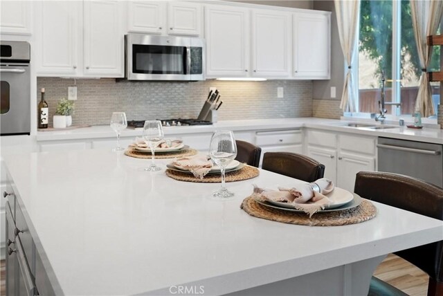 kitchen with decorative backsplash, a breakfast bar, white cabinets, and appliances with stainless steel finishes