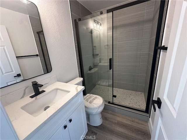 bathroom with hardwood / wood-style floors, vanity, toilet, and a shower with door