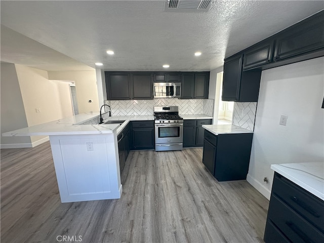 kitchen with tasteful backsplash, kitchen peninsula, a textured ceiling, appliances with stainless steel finishes, and light wood-type flooring