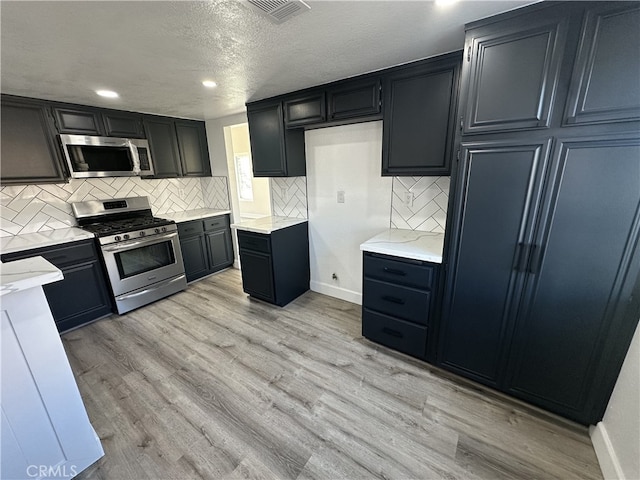 kitchen with backsplash, light hardwood / wood-style flooring, stainless steel appliances, and a textured ceiling